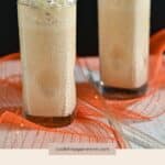 Two tall glasses of Pumpkin Milkshake, topped with whipped cream, sit on an orange cloth, capturing the essence of the season.