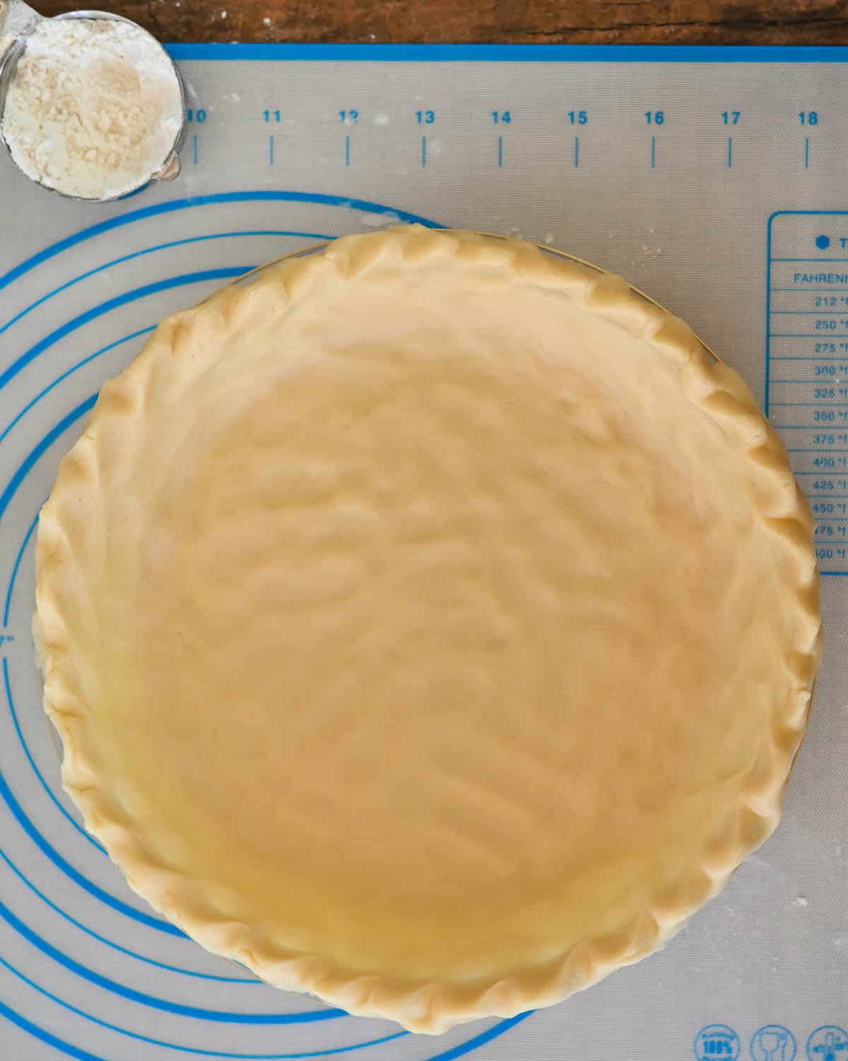 Pie dough in a baking dish next to a cup of flour. 