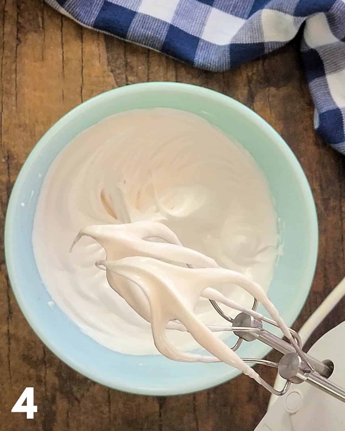 Egg whites with stiff peaks being shown on mixer beaters.