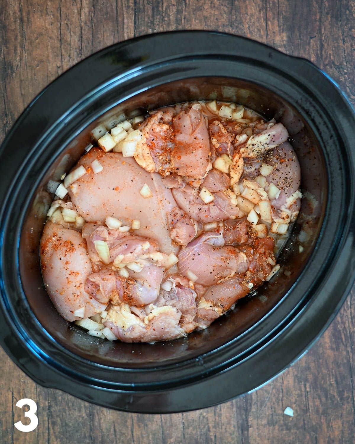 Onion, raw chicken, and spices in a crock pot.