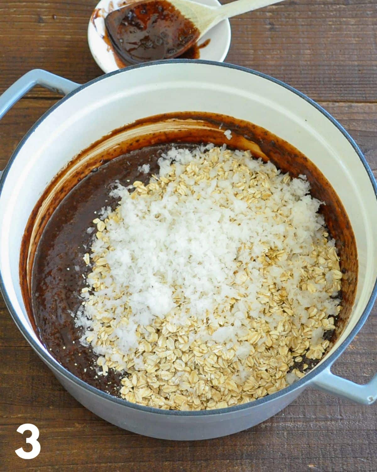 Oats and coconut being added to warm chocolate cookie mix.