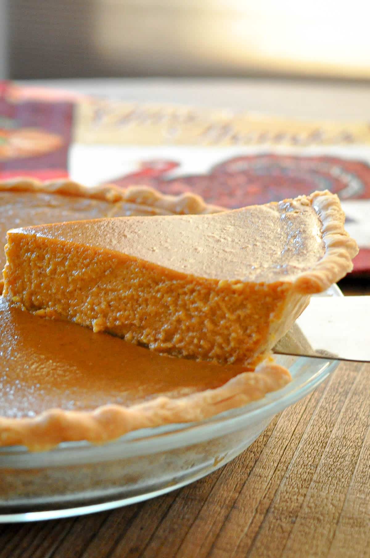 A slice of Butternut Squash Pie is being lifted from a glass pie dish on a wooden surface.