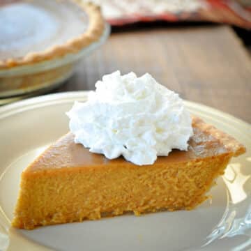 A slice of Butternut Squash Pie topped with whipped cream on a plate.