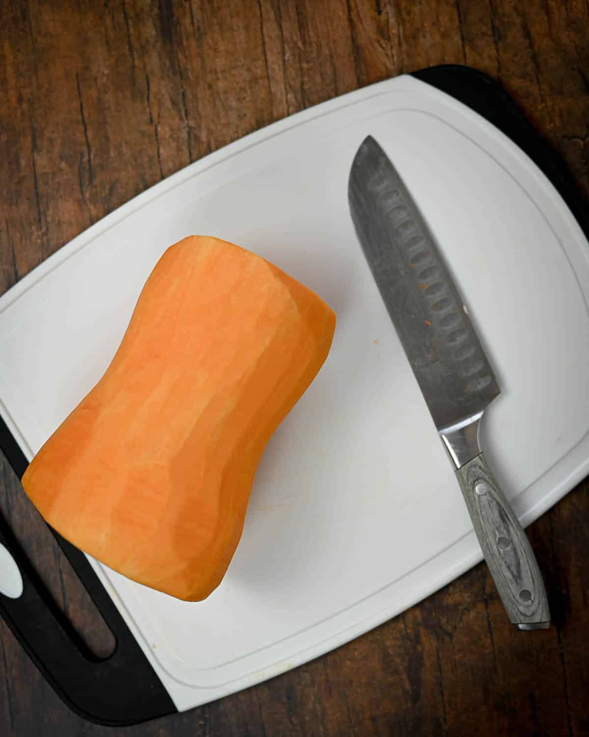 Peeled butternut squash and a knife on a white cutting board, ready for your next Butternut Squash Pie recipe, placed on a wooden surface.