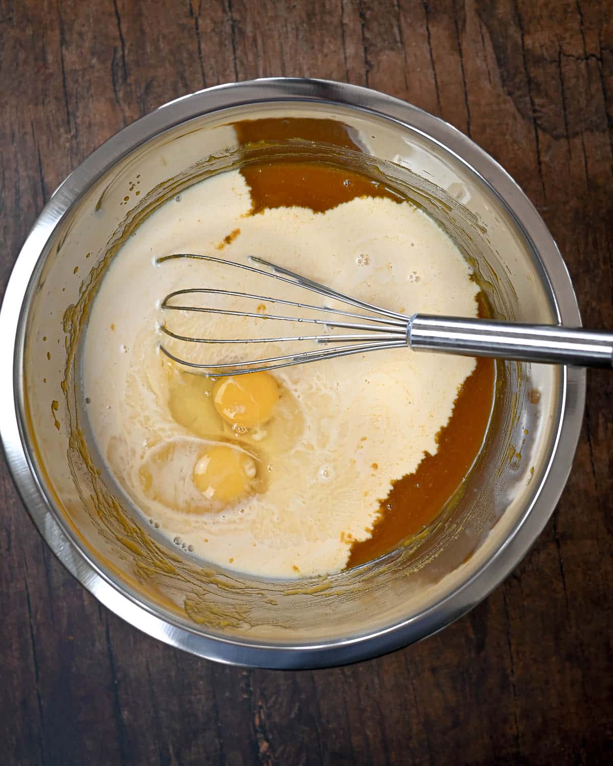 A mixing bowl with eggs, milk, and pumpkin puree being whisked on a wooden surface-perfect for starting your Butternut Squash Pie recipe.