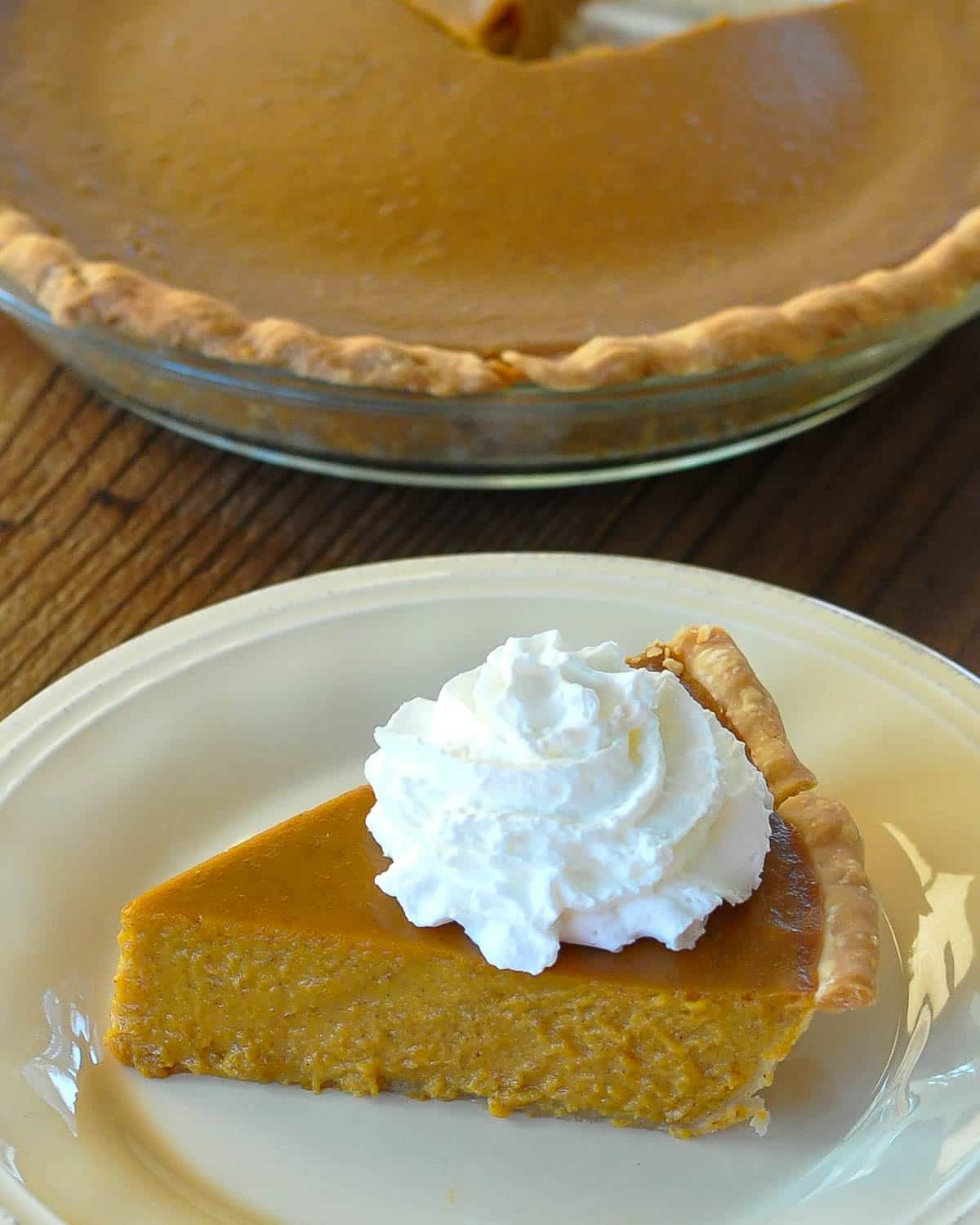 A slice of butternut pie with whipped topping on a cream colored plate. 
