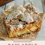 A slice of Easy Apple Cake dusted with powdered sugar rests on parchment paper, with more cake in the background.