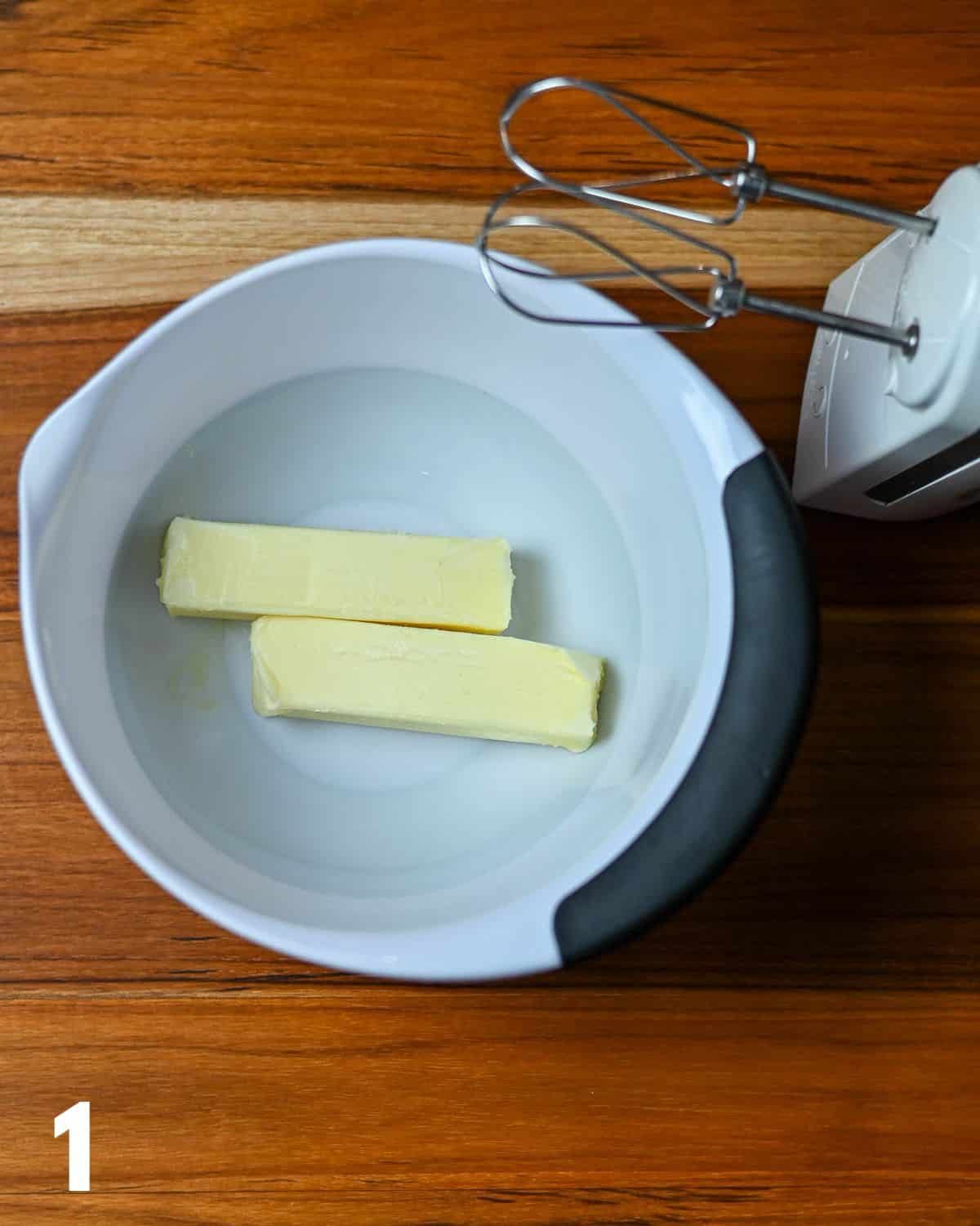 Two sticks of butter in a white mixing bowl. 