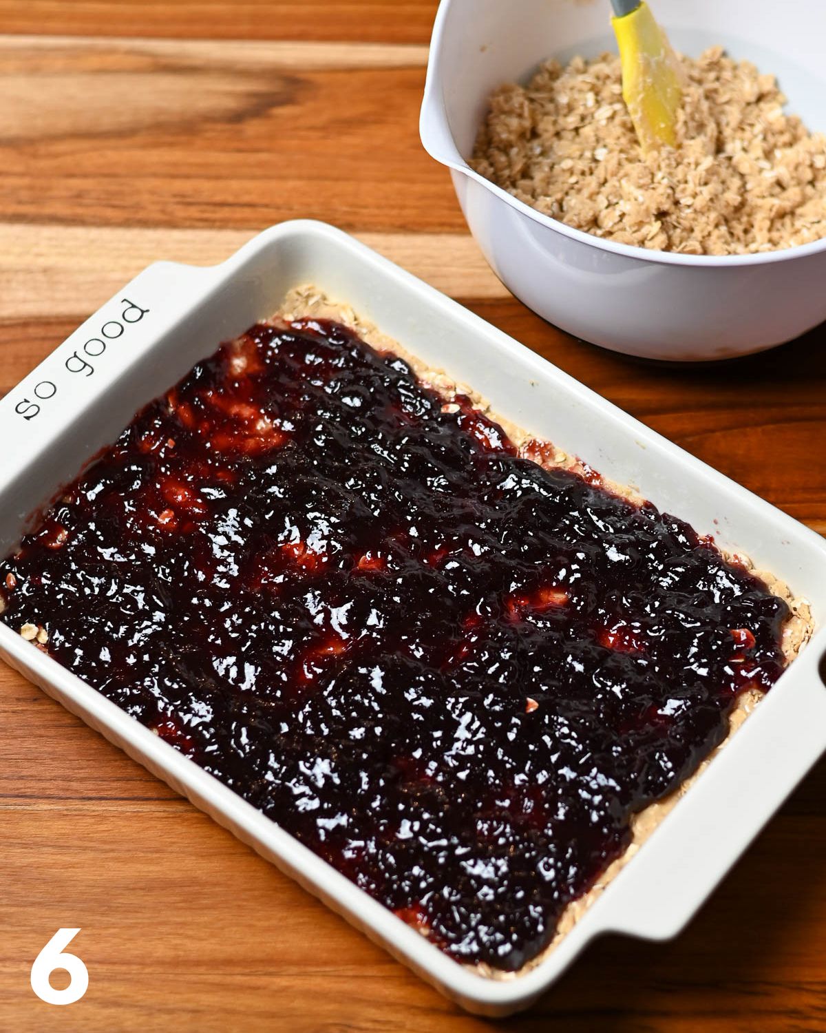 Jam spread over a oatmeal cookie base in a baking dish. 