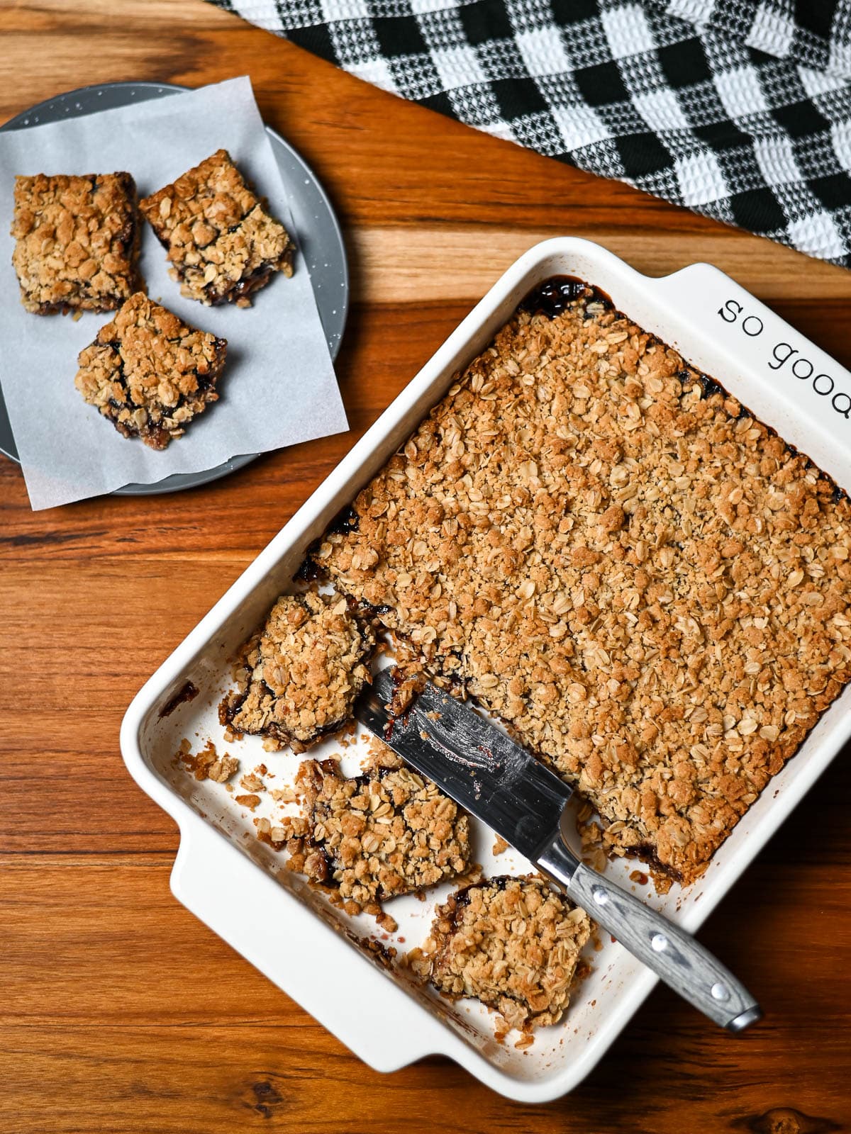 Oatmeal and jam cookie bars in a white baking dish next to a plate of jam bars.