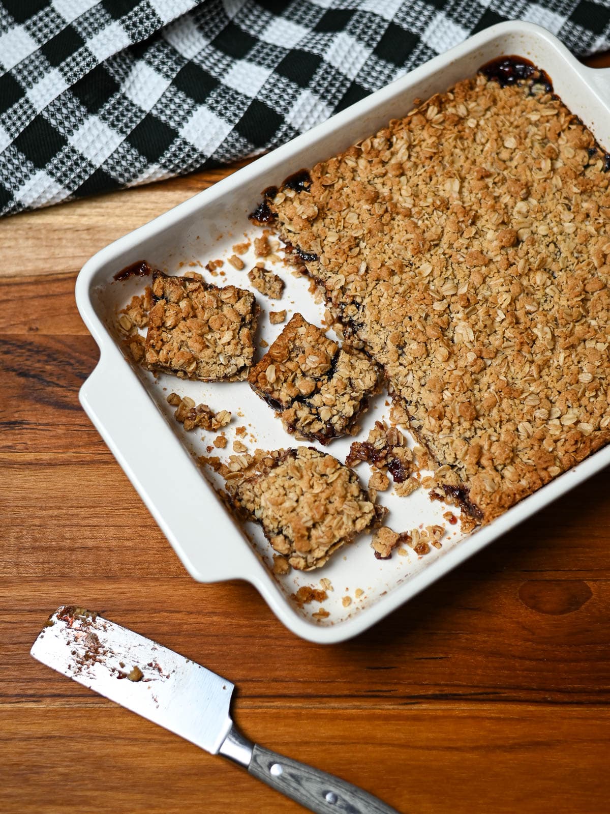 Oatmeal and jam cookie bars in a white baking dish next to a plate of jam bars.