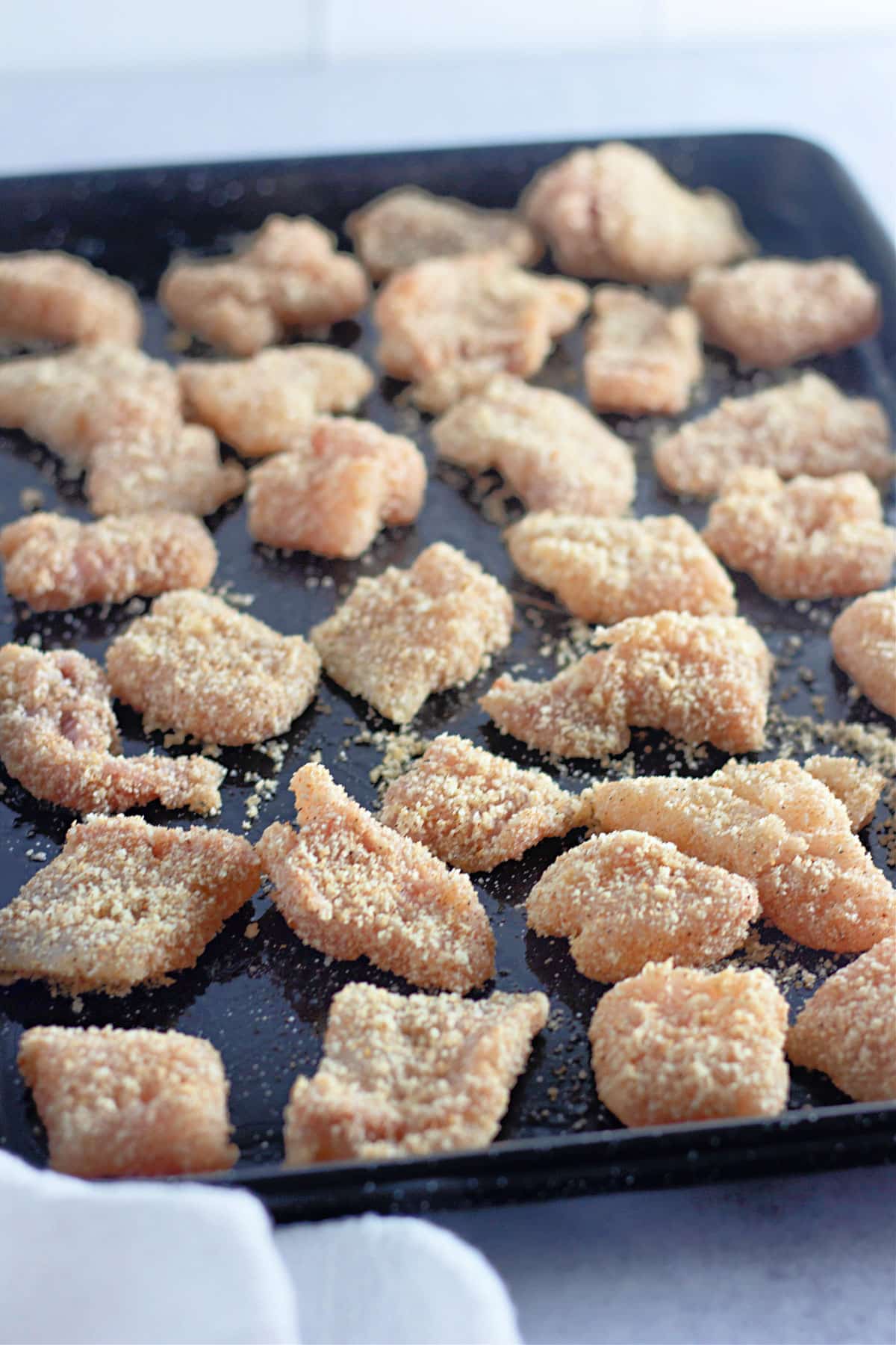 Raw catfish pieces covered with panko on a baking sheet. 