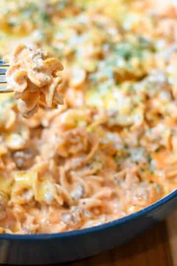 Cheese lasagna on a fork with the skillet of lasagna behind. it.