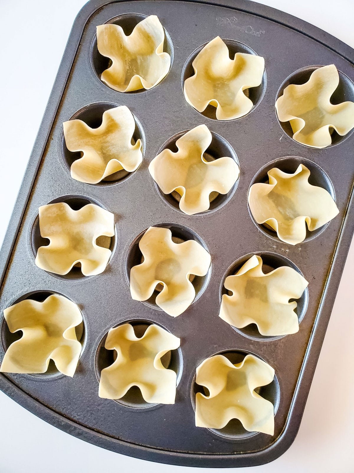 Wonton wrappers placed in a muffin pan.