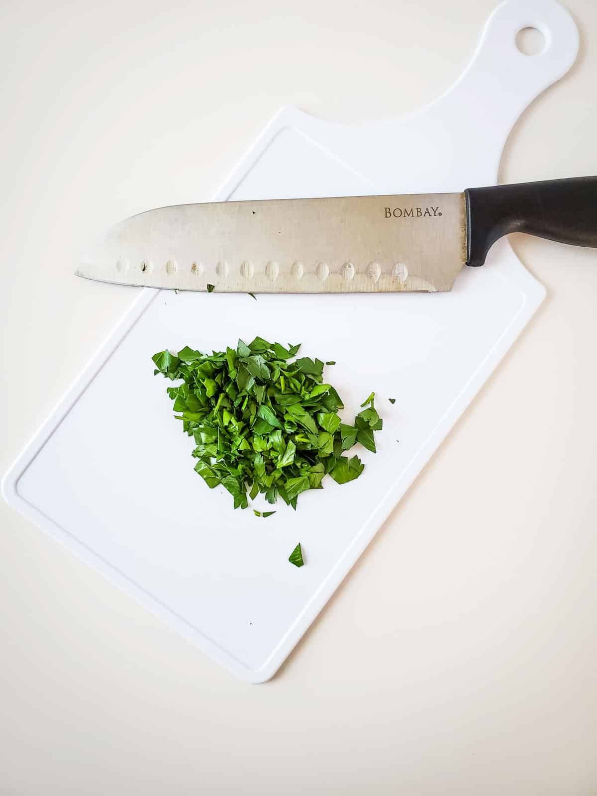 Chopping parsley on a white cutting board next to a knife. 