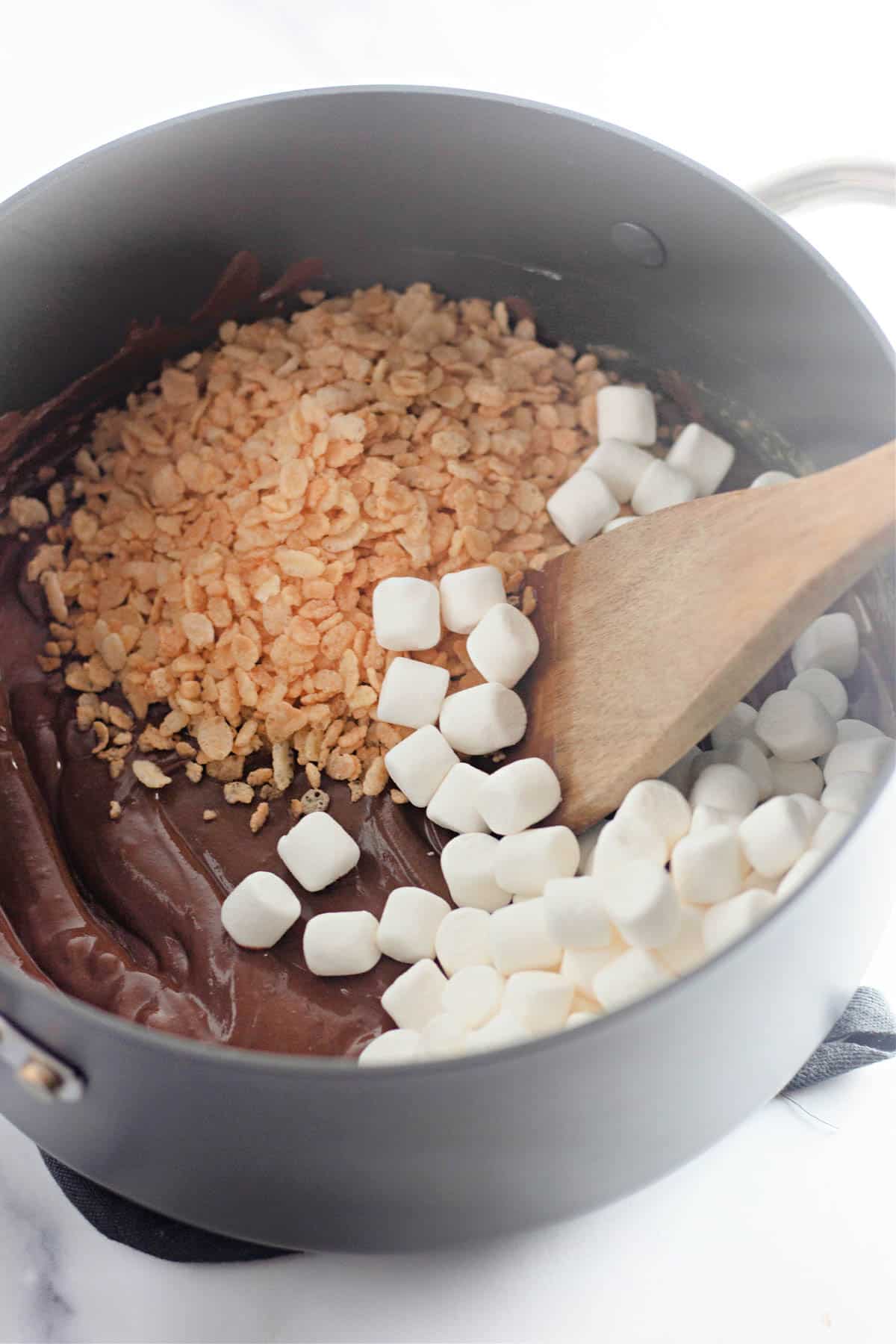 Melted chocolate, rice krispys, and marshmallows in a saucepan.