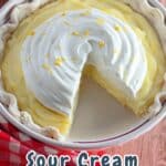 A sliced Sour Cream Lemon Pie with whipped topping and lemon zest sits on a wooden table covered by a red checkered cloth.