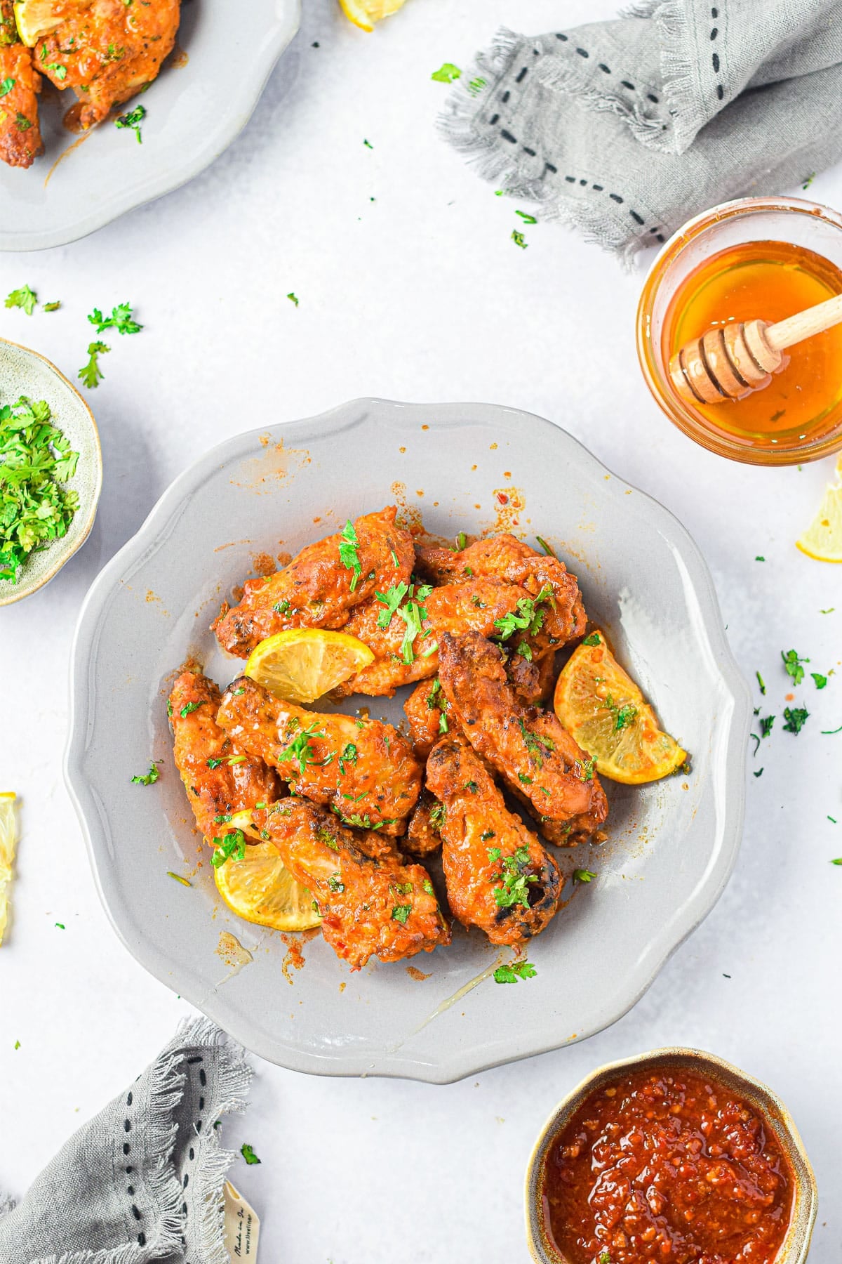 Air Fryer Honey Lime Chicken Wings coated in sauce, garnished with lemon slices and herbs, are served on a gray plate with sides nearby.