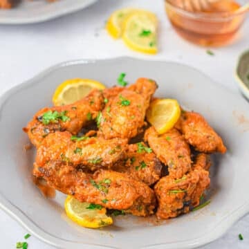 Plate of saucy Air Fryer Honey Lime Chicken Wings garnished with lemon slices and chopped herbs.