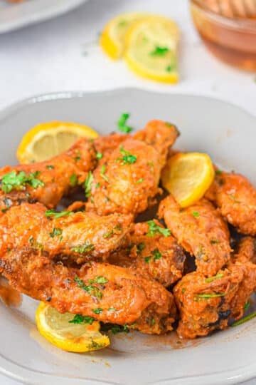 Plate of saucy Air Fryer Honey Lime Chicken Wings garnished with lemon slices and chopped herbs.