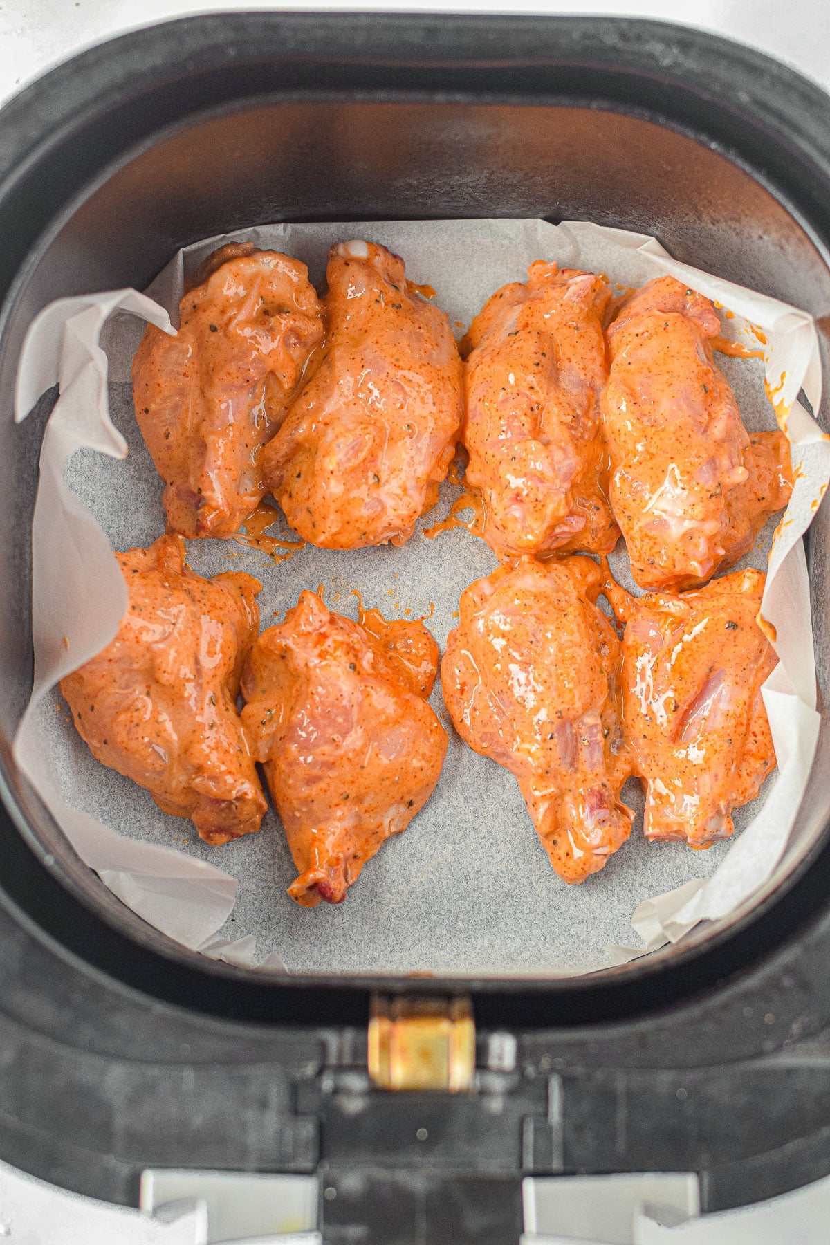 Eight raw, batter coated Honey Lime Chicken Wings are arranged on parchment paper in an air fryer basket.
