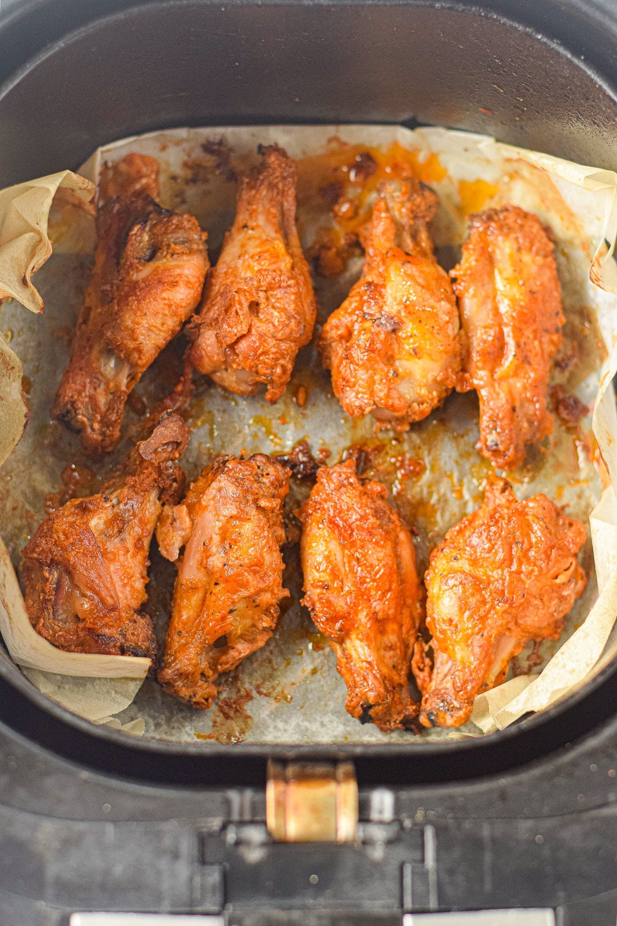 Eight cooked Air Fryer Honey Lime Chicken Wings in an air fryer basket lined with parchment paper.