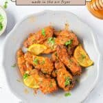 Air Fryer Honey Lime Chicken Wings with lime slices and herbs are arranged beautifully on a plate, accompanied by a honey dipper and flavorful sauces nearby, with the recipe title displayed at the top.