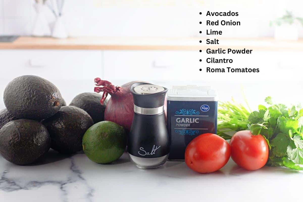Avocados, red onion, lime, salt, garlic powder, cilantro, and roma tomatoes on a kitchen counter—perfect ingredients for an Easy Guacamole Recipe.