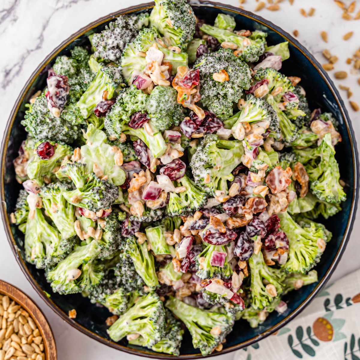 Broccoli Salad in a black bowl next to sunflower seeds.