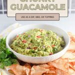 Bowl of chunky guacamole brimming with diced vegetables, surrounded by crispy tortilla chips and fresh cilantro.