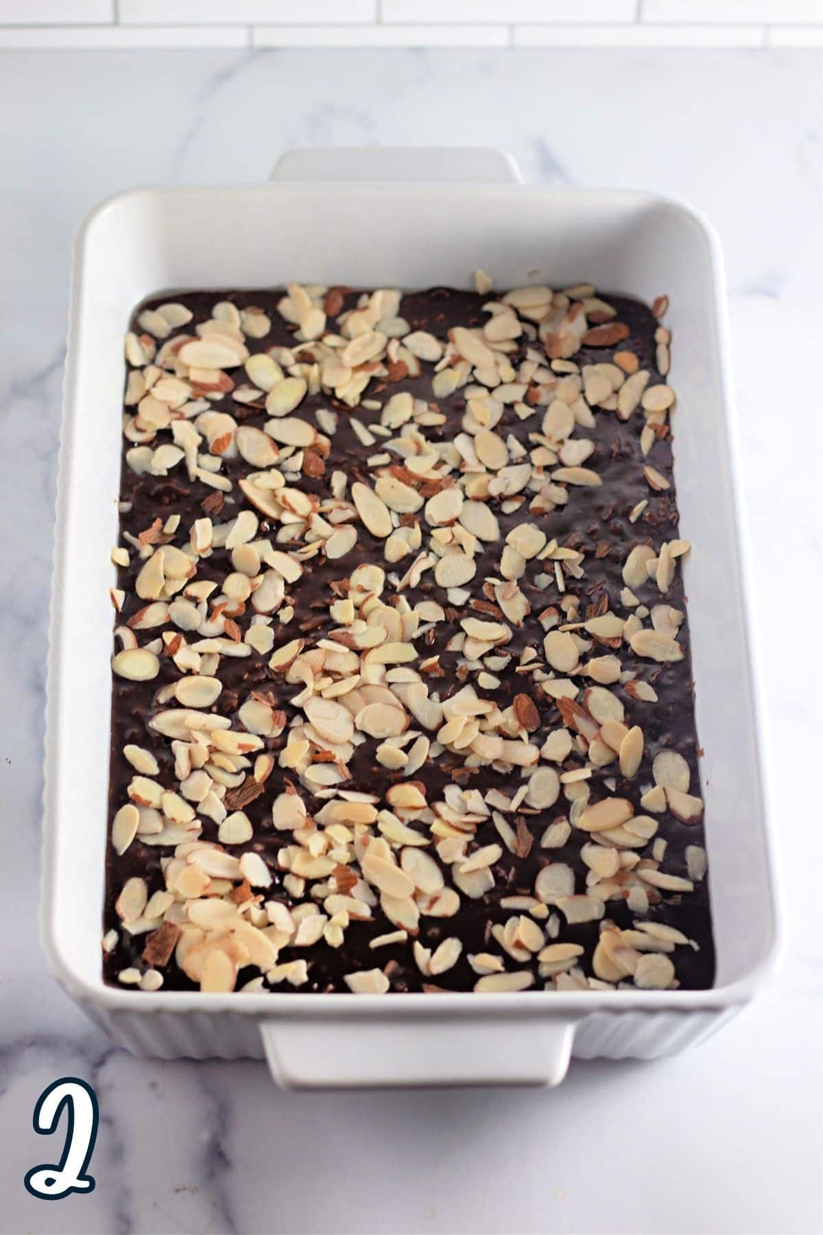 Brownie batter in a white baking dish topped with slivered almonds. 