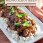 Easy Mongolian Beef with onions and peppers served over rice on a white platter, garnished with green onions.