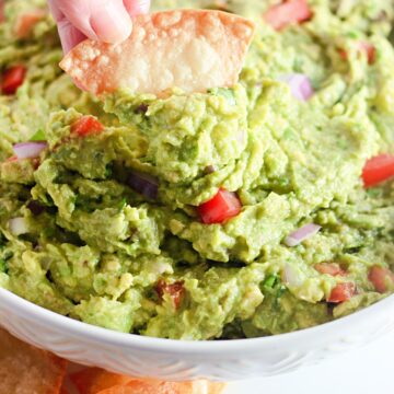 A tortilla being dipped in guacamole.