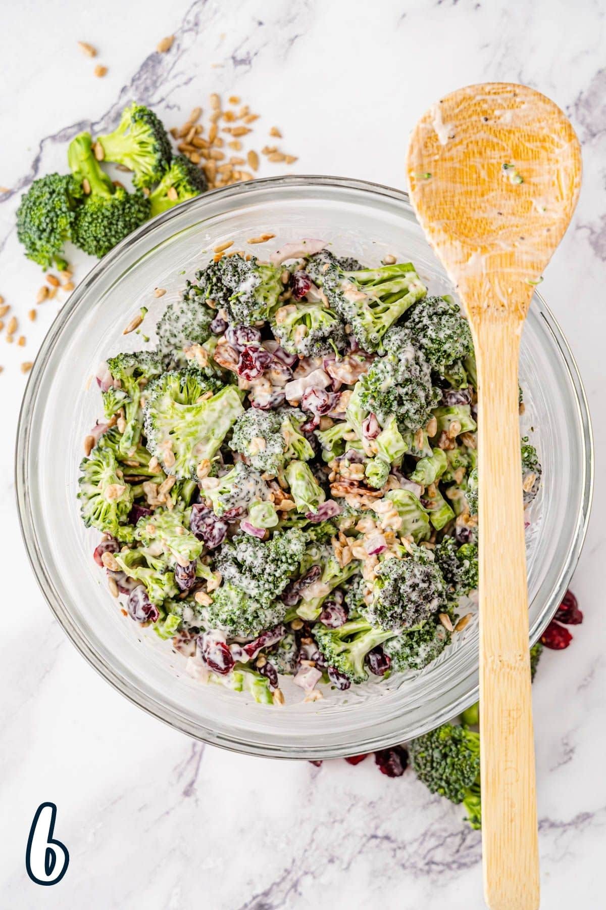 Just mixed broccoli salad in a glass bowl with a wooden spoon. 