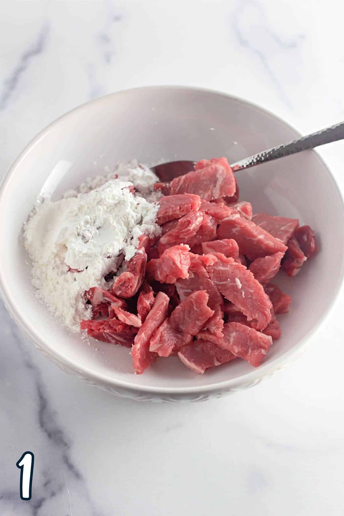 Strips of raw steak and cornstarch in a bowl. 