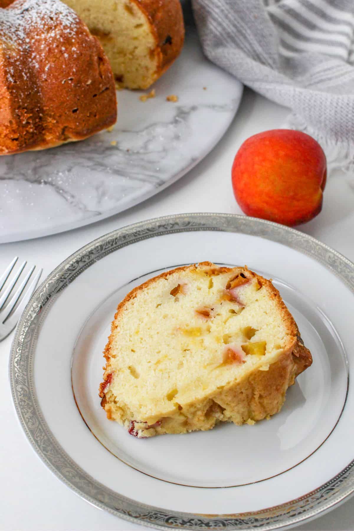 A slice of peach cake on a plate next to a peach and the rest of the cake. 