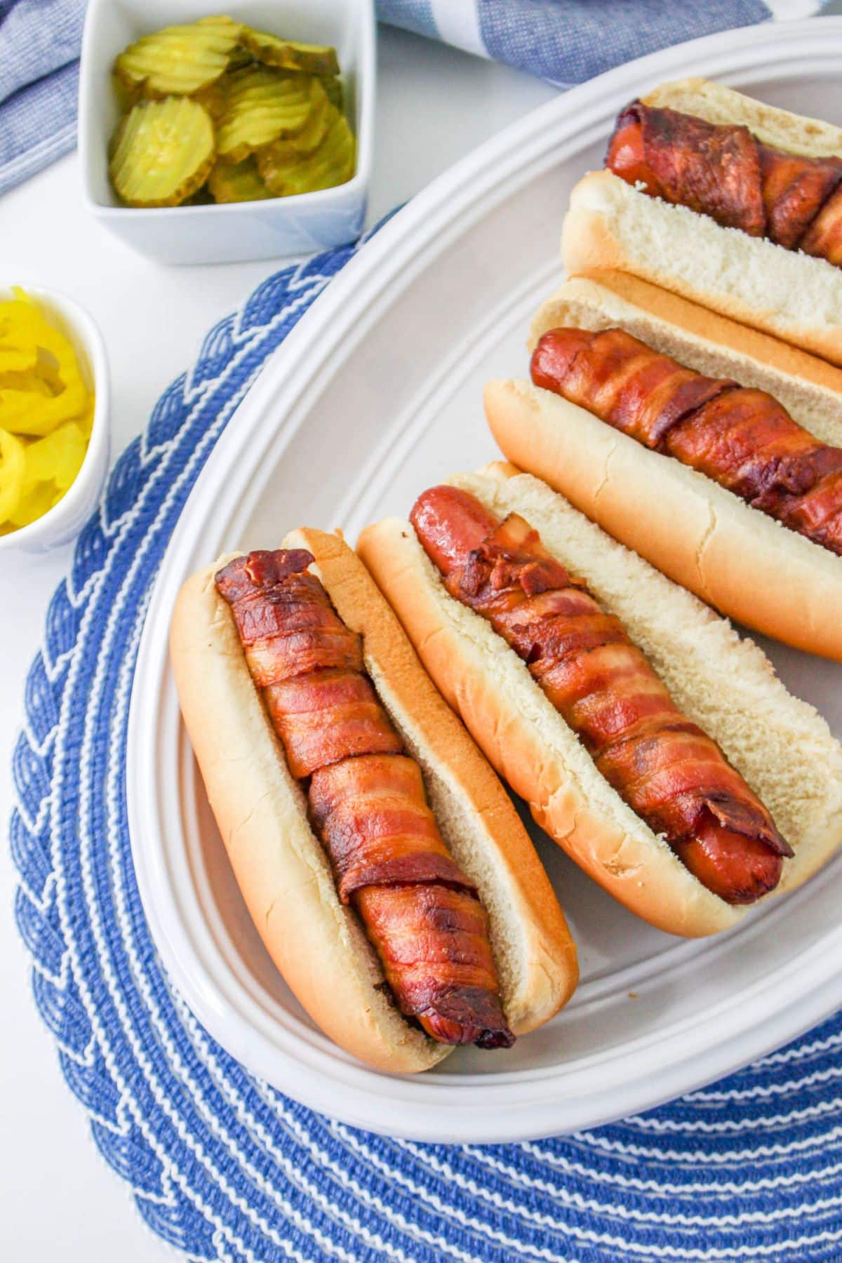 Hot dogs wrapped in crispy bacon in a bun on a white plate. 