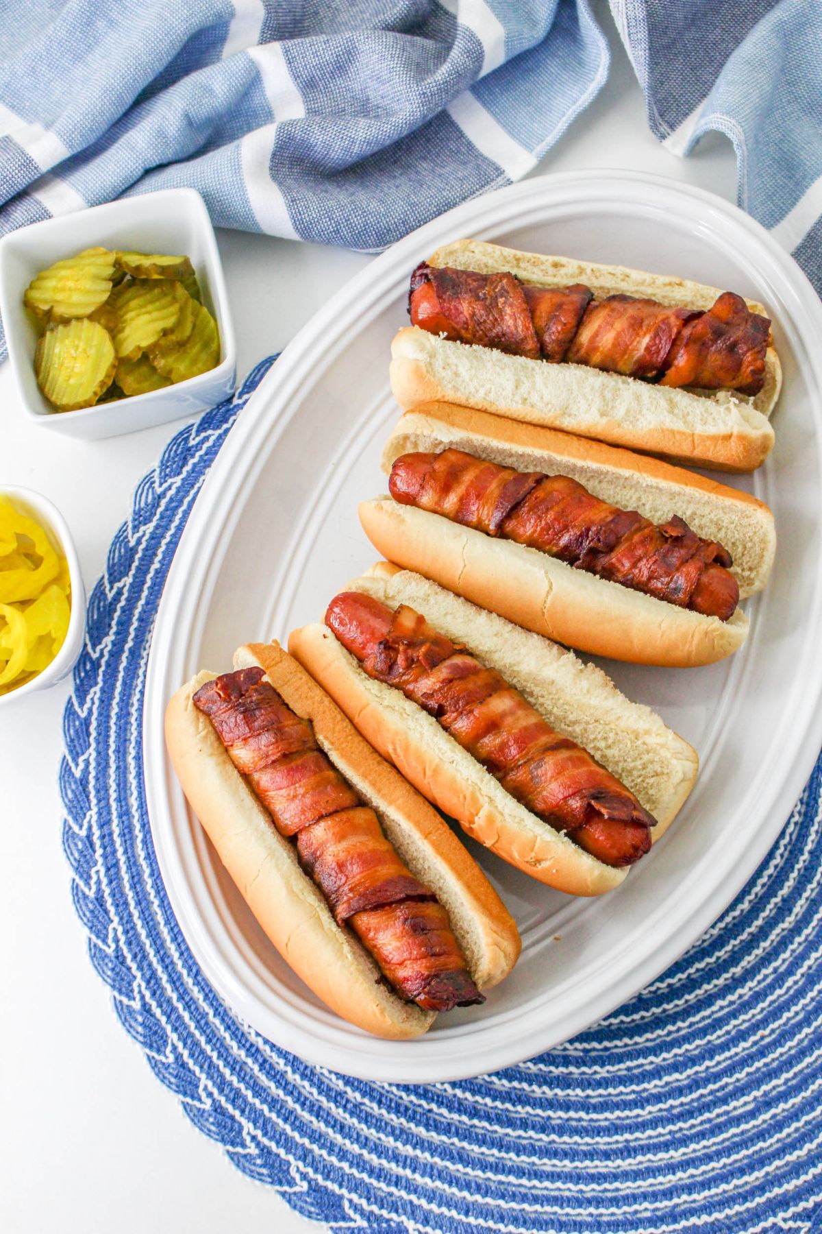 Bacon dogs in a bun on a white plate.