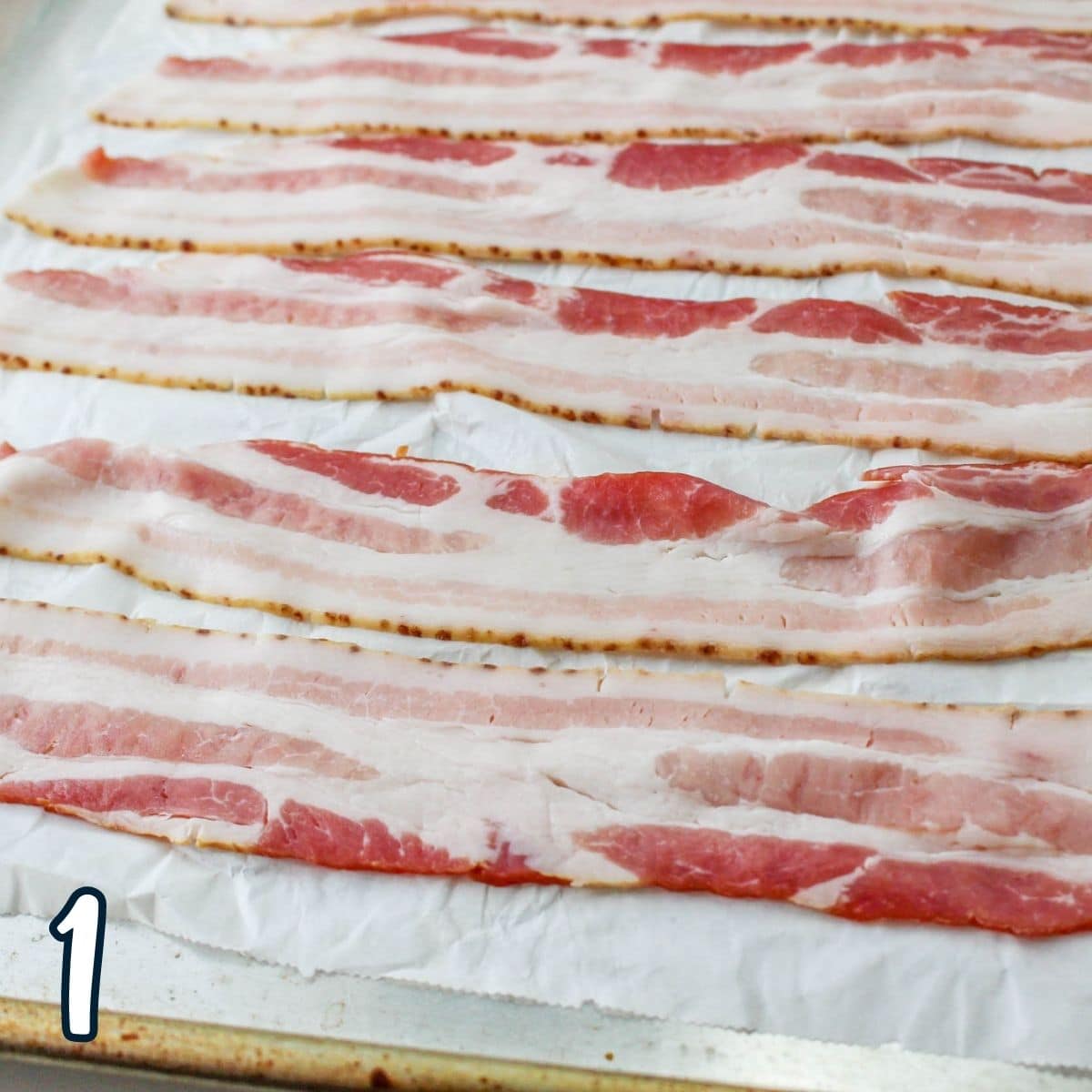 Raw bacon on parchment paper on a baking sheet.
