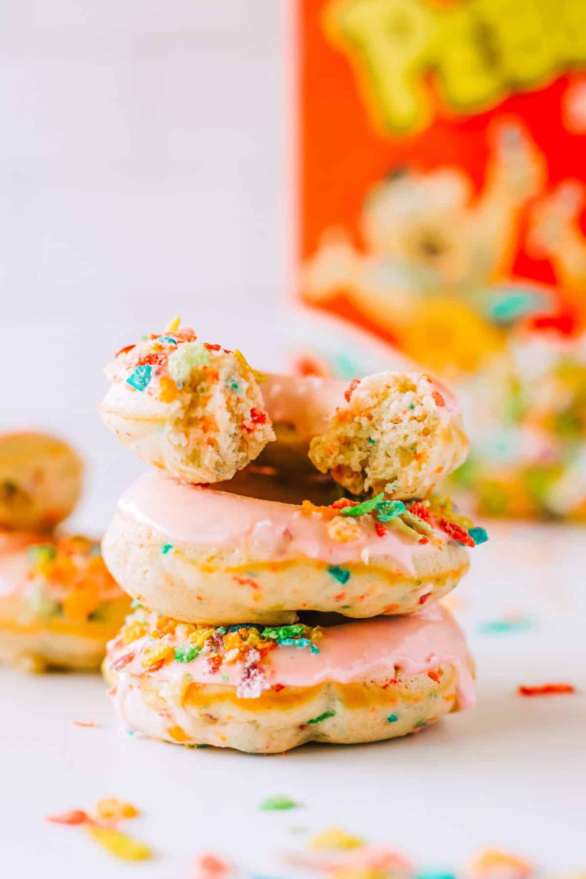 A stack of donuts with pink frosting and fruity pebble cereal topping. 