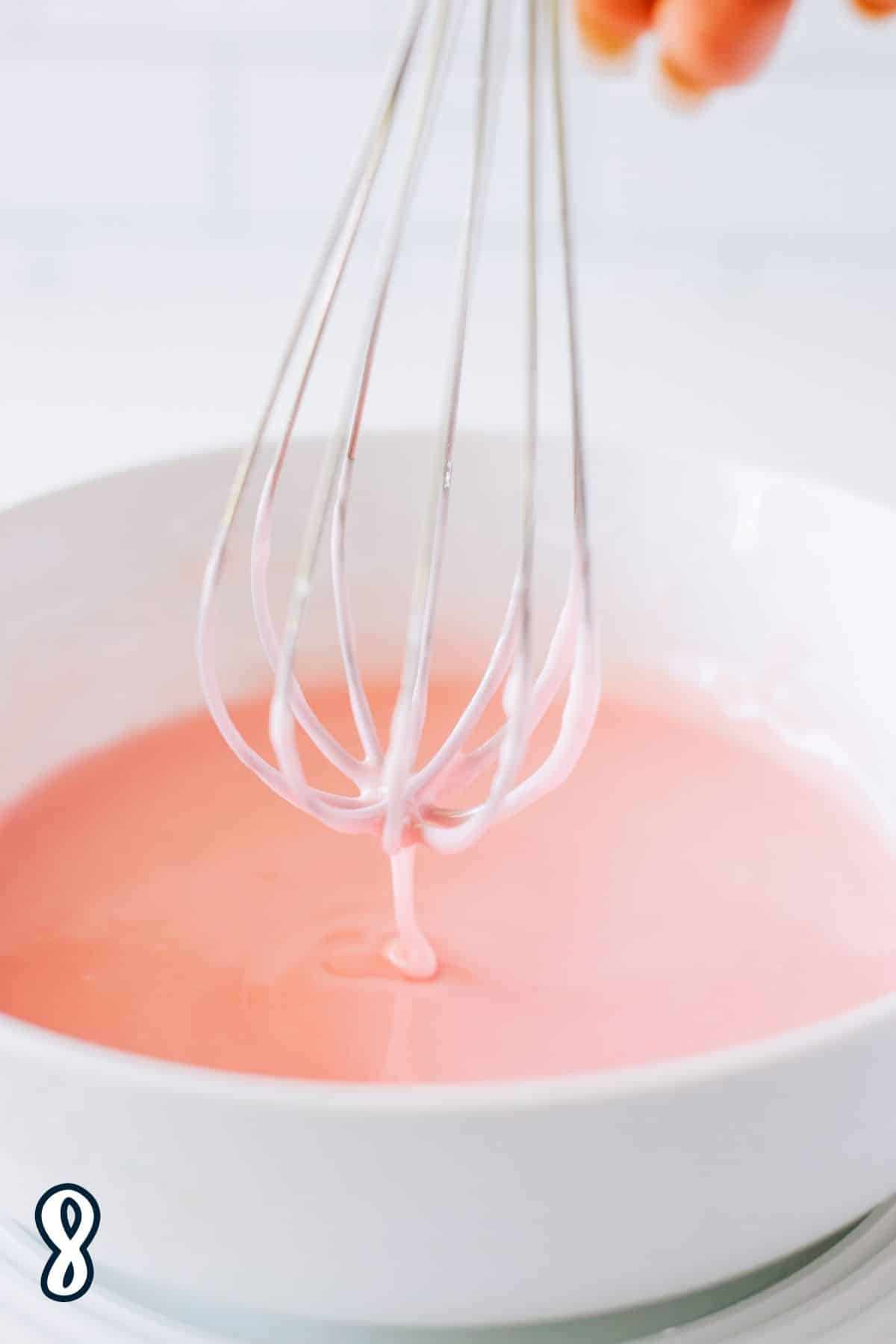 A whisk hovering over just mixed strawberry glaze. 