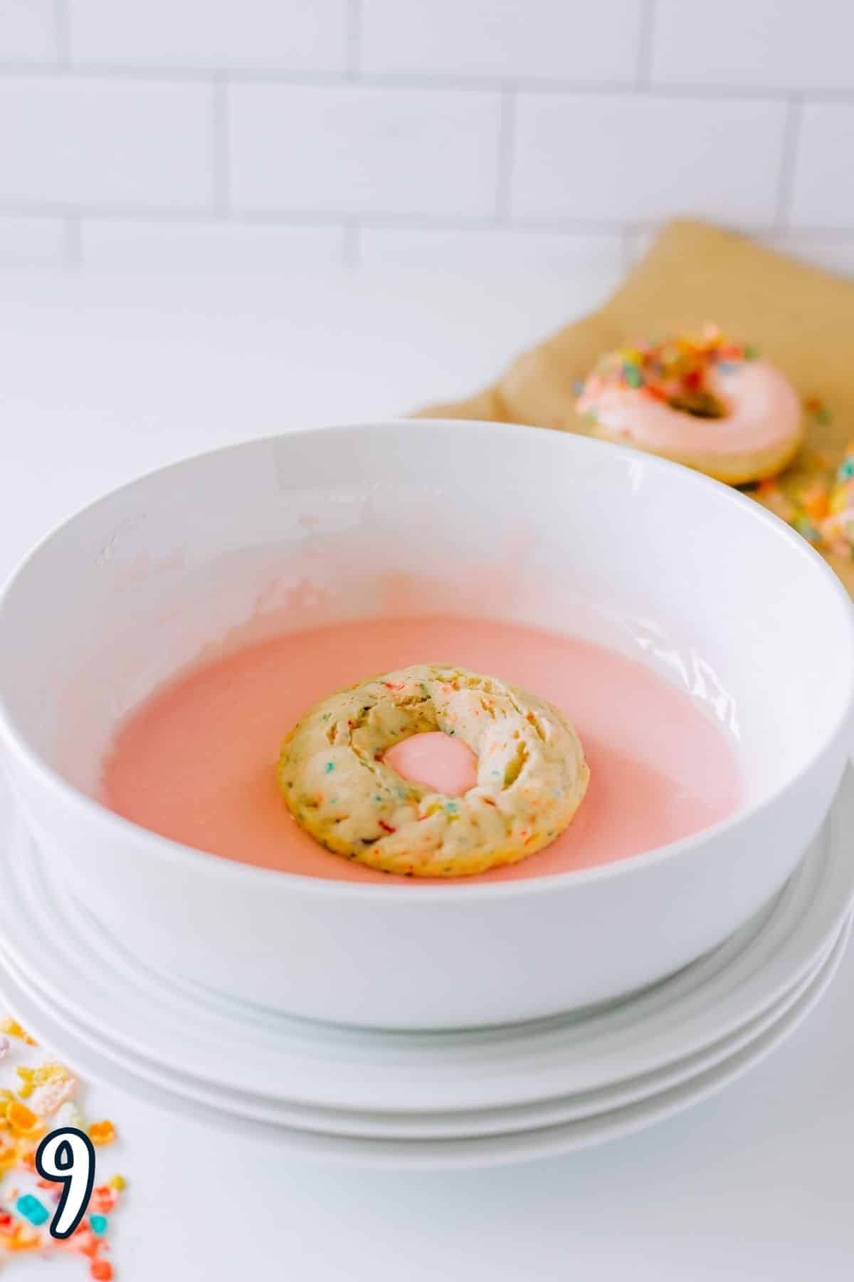 A donut being dipping into strawberry glaze. 