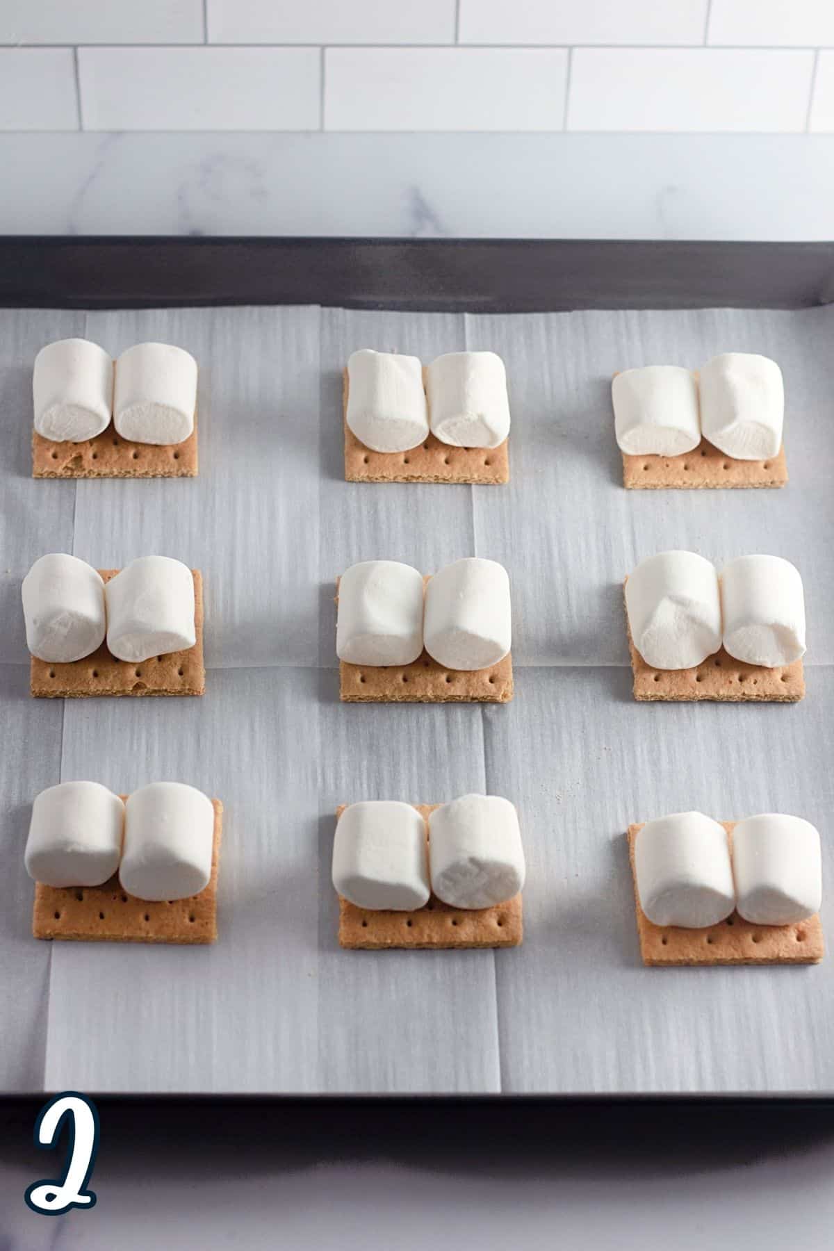 Marshmallows on top of graham crackers on a baking sheet. 