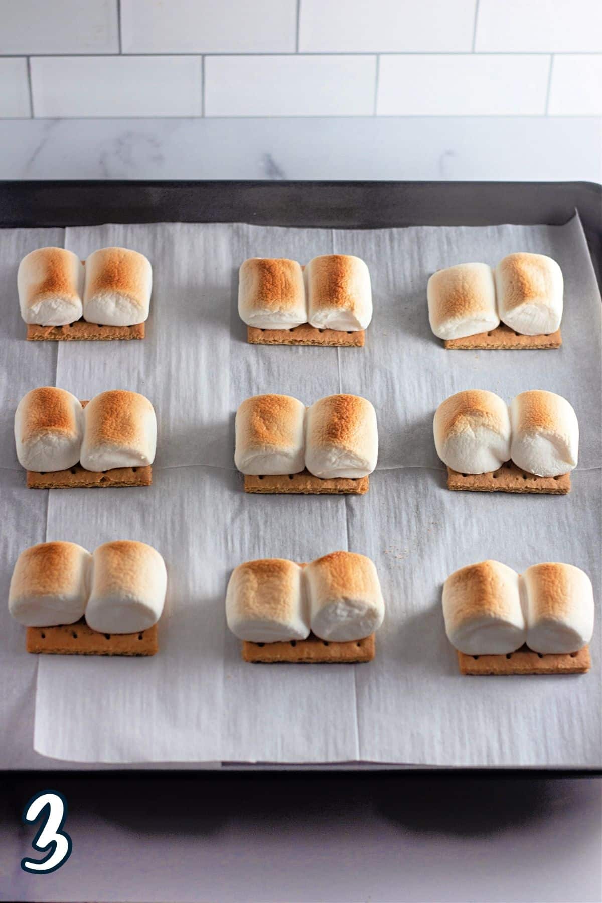 Toasted marshmallows on graham crackers on a baking sheet. 