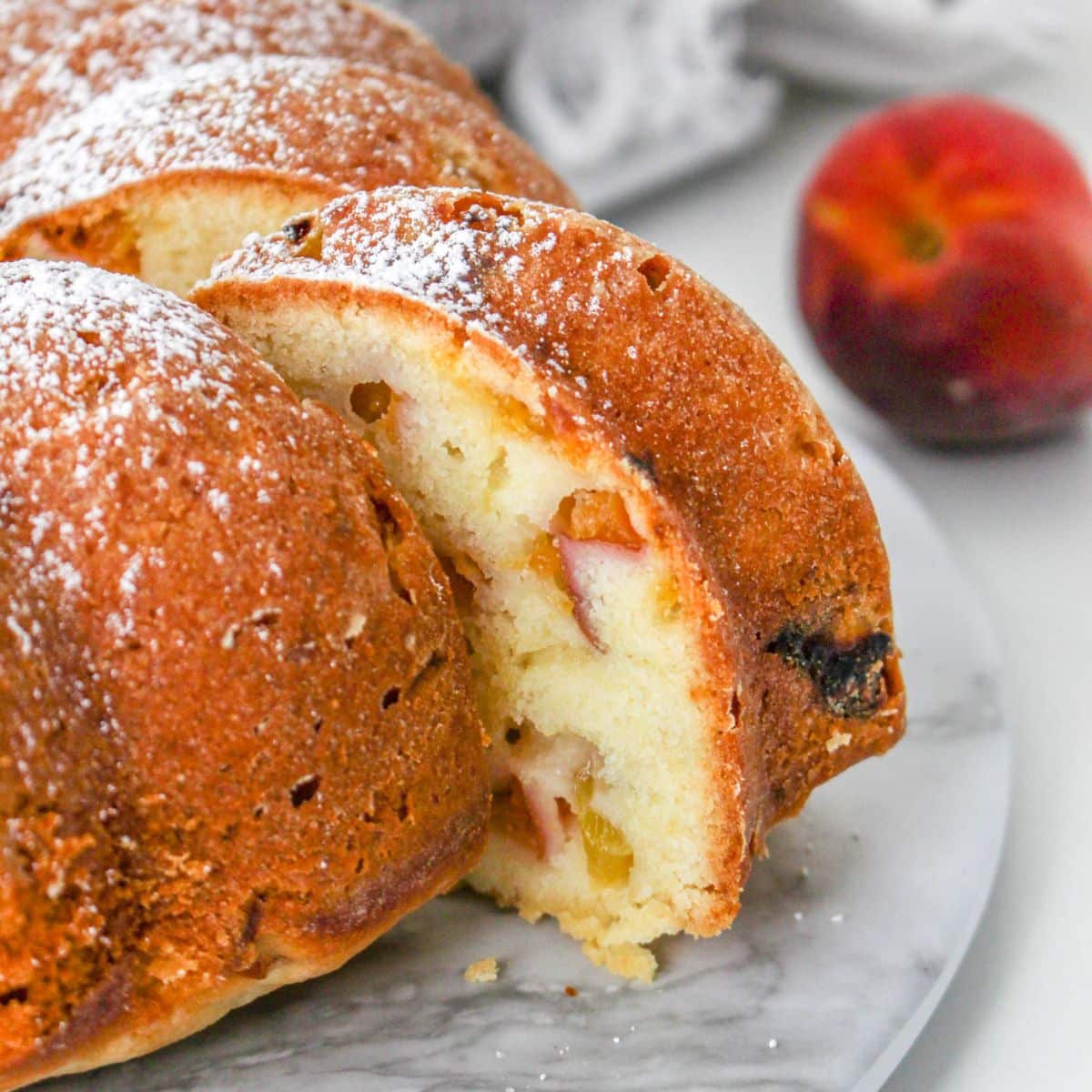 A peach bundt cake on a marble cake platter with one piece sliced.