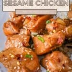 Close-up of Slow Cooker Sesame Chicken garnished with sesame seeds and green onions on a white plate.
