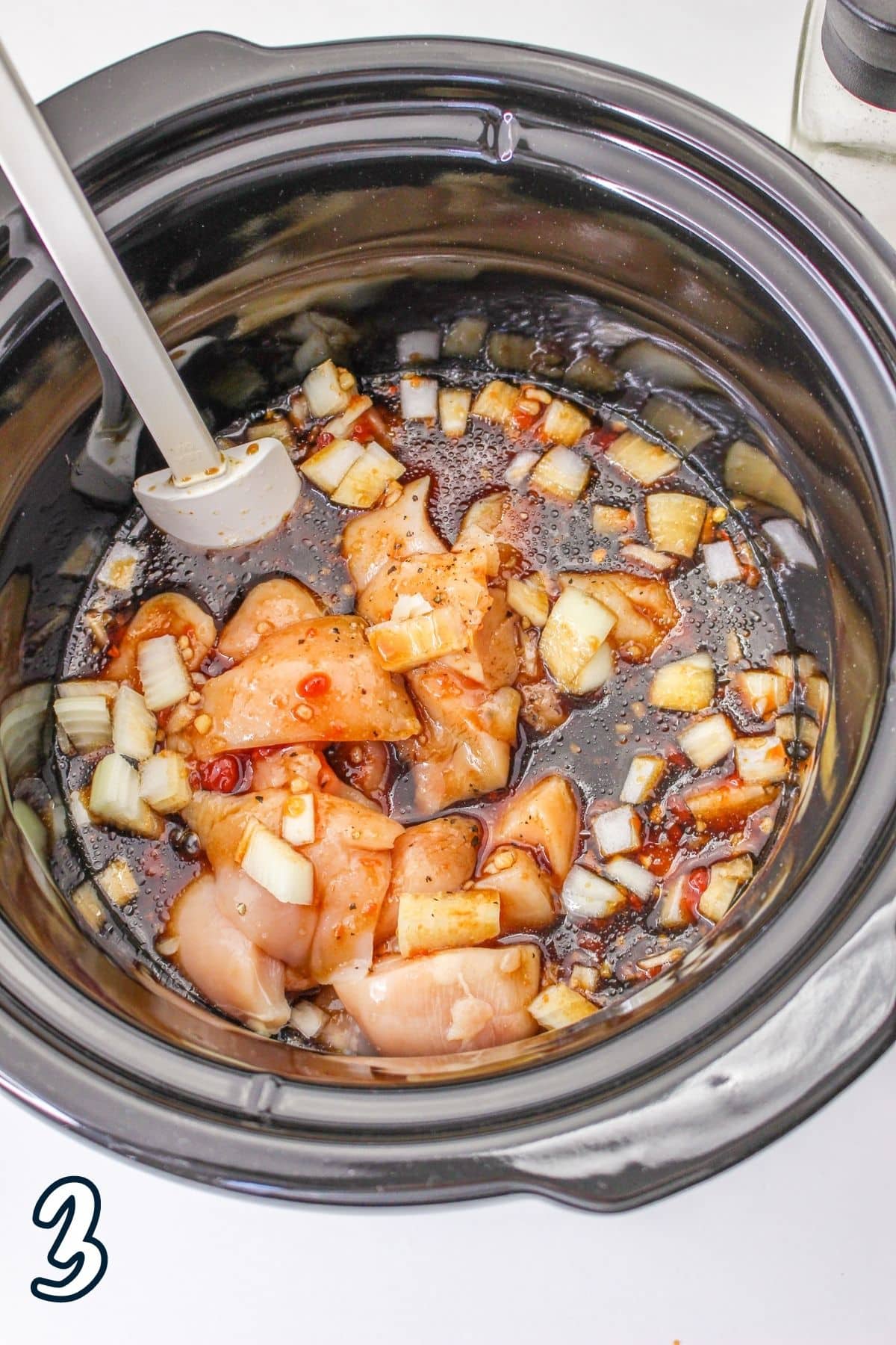 Sesame sauce poured over raw chicken in a crock pot bowl ready to cook. 