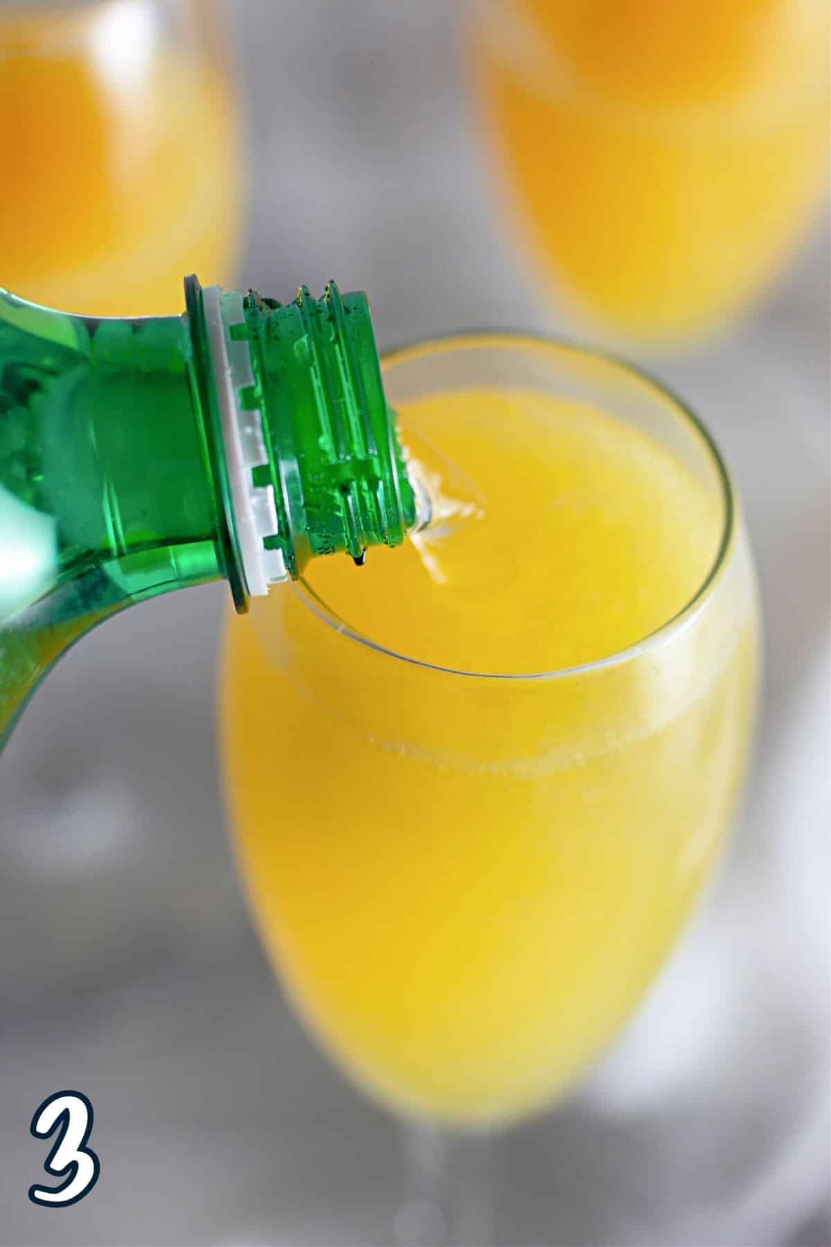 Lemon-lime soda being poured over orange juice in a champagne glass. 