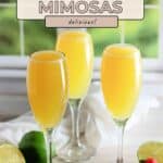 Three glasses of refreshing Virgin Mimosas with limes and strawberries sit on a table, bathed in sunlight from a bright window in the background.