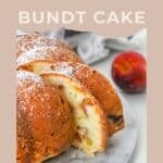 Sliced Peach Bundt Cake on a plate with powdered sugar, whole peach in the background.